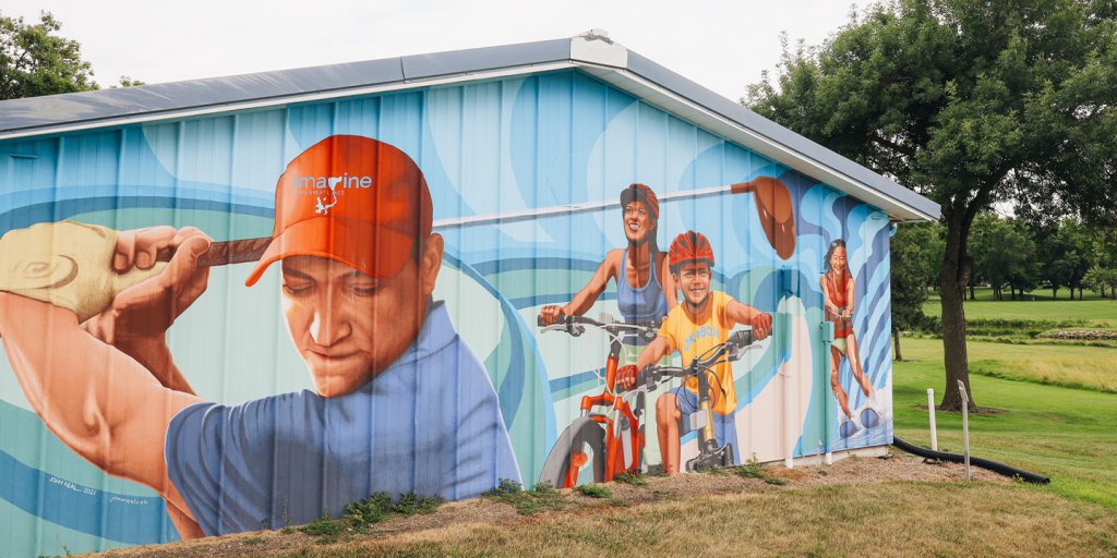 A mural of a man golfing, a mom and child biking, and a woman skiing on the side of a building.