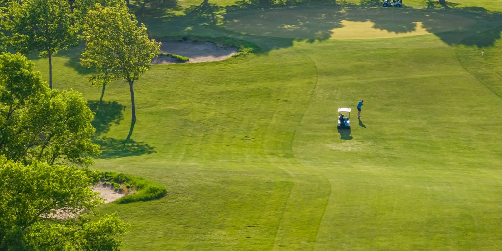 Why Business Retreats in Okoboji are the ultimate event experience 7 A golf cart on a green with a golfer teeing off.