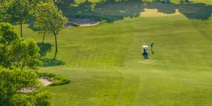 A golf cart on a green with a golfer teeing off.