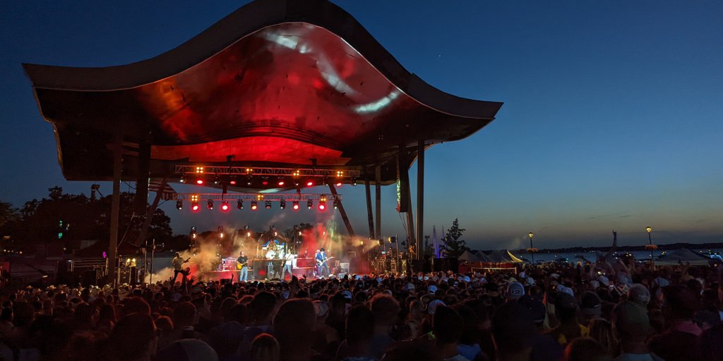 A group of people watching an outdoor concert at night, the stage is bathed in red light.