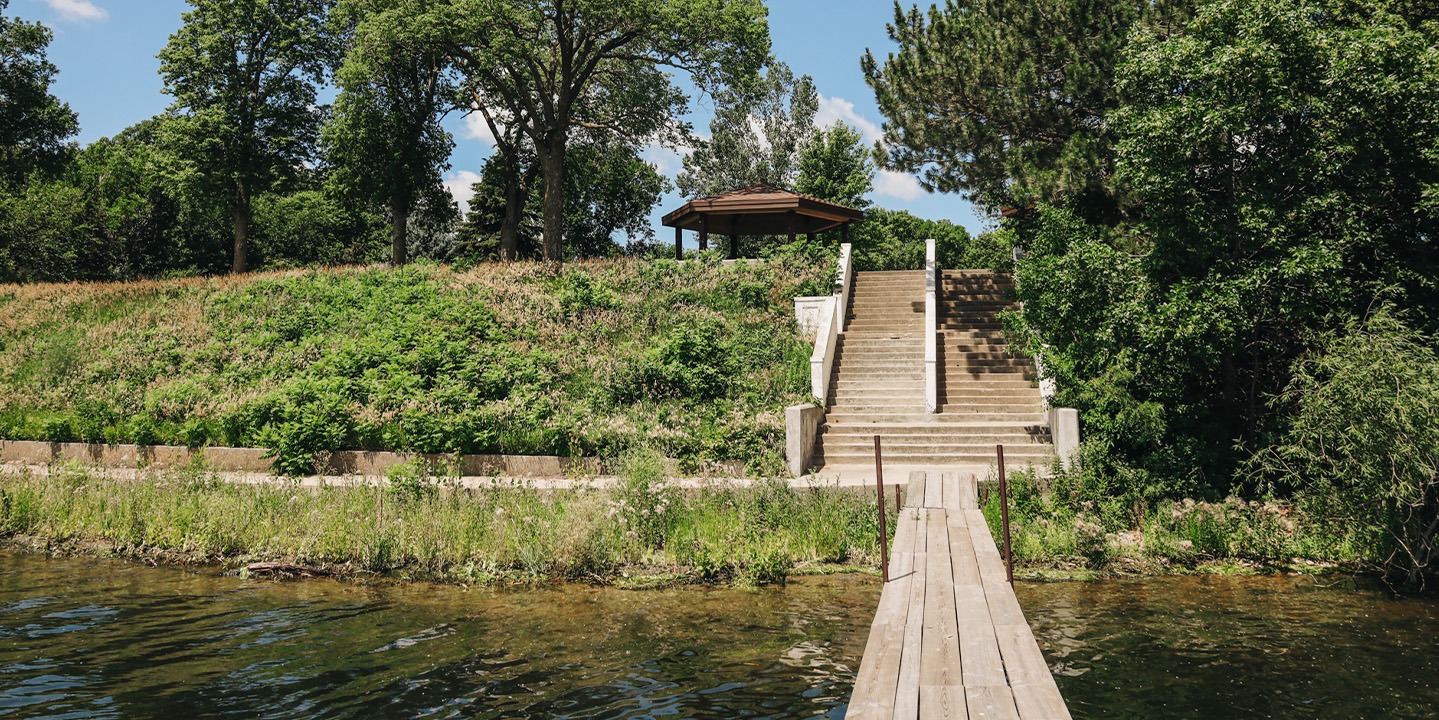 Parks 2 A wooden walkway over a body of water with a gazebo and trees