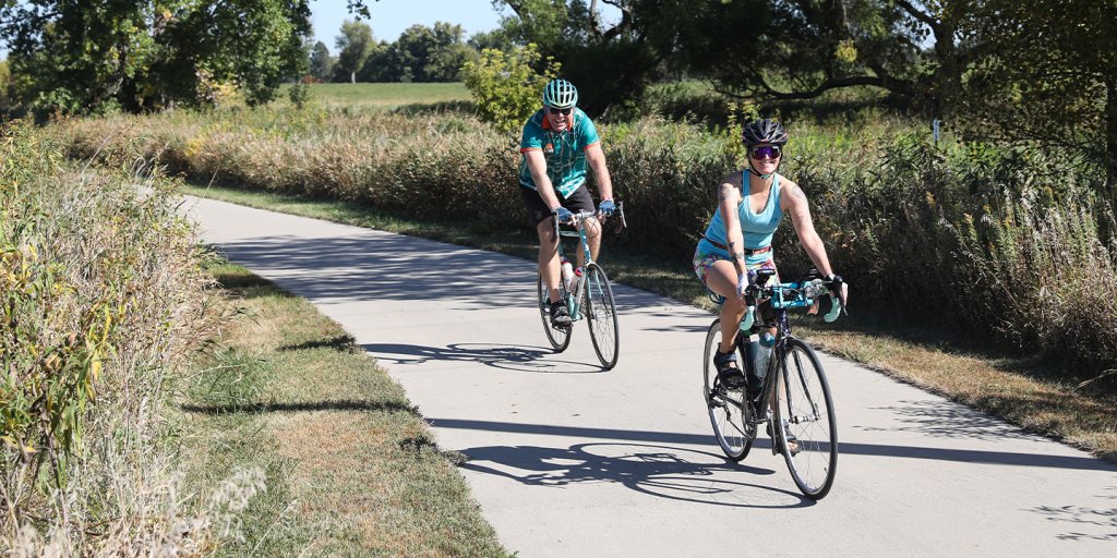 A man and woman riding bicycles on a path wearing biking helmets.