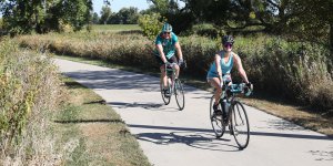 A man and woman riding bicycles on a path wearing biking helmets.