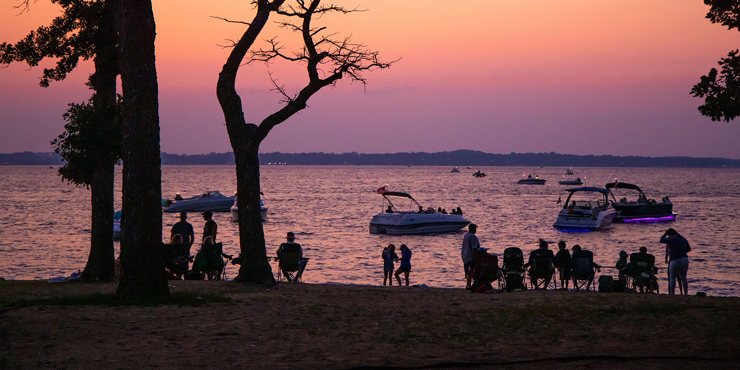 Okoboji Webcams 2 People sitting on the beach or in boats on the water at sunset